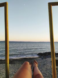 Low section of man relaxing on beach against clear sky