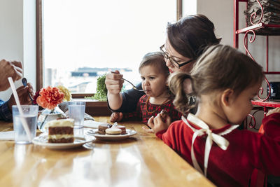 Mother feeding girl while sitting family at restaurant table