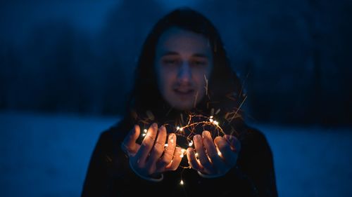 Portrait of young woman holding illuminated lighting equipment at night