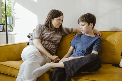 Serious woman consoling son while sitting on sofa at home