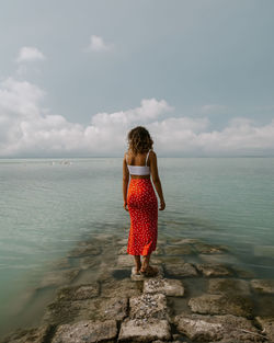 Rear view of woman standing by sea against sky