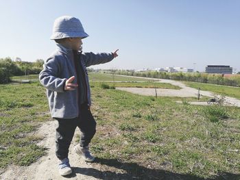 Boy pointing while standing on field during sunny day