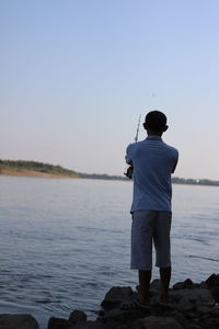 Rear view of man fishing in lake during sunset