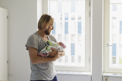 Side view of woman standing against window at home