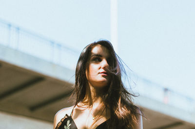 Low angle view of smiling beautiful woman with bridge in background