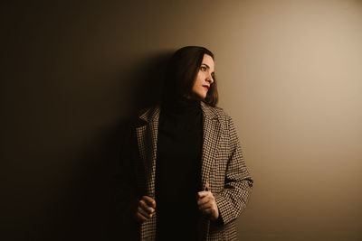 Young woman looking away while standing against wall