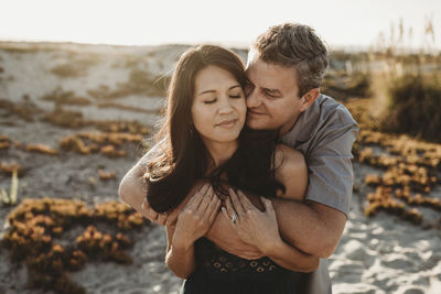 Mid-40's husband embraces beautiful wife with sand dune in background