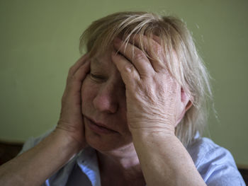 Sad woman with head in hands against green wall at home