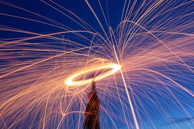 Low angle view of man spinning wire wool against sky at night