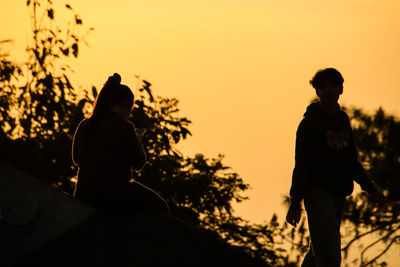Silhouette man and woman standing against sky during sunset