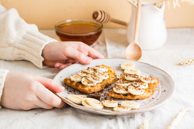 Children's hands hold a plate of sandwiches with honey, banana and chocolate on the table. 