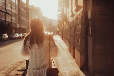 Rear view of woman walking on street in city at sunset