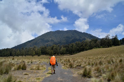 Rear view of man walking on mountain against sky