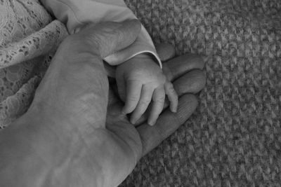 Cropped image of man holding child hand on bed