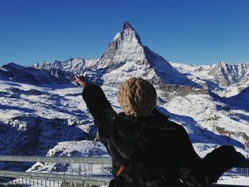 Rear view of woman gesturing towards snowcapped mountain against sky