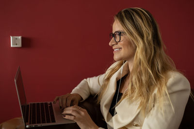 Woman working at home with laptop classic brown arm chair. red  wall home office. gray notebook 