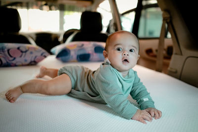 A 6 months old baby looking at the camera while laying on a bed in a campervan