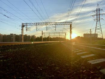 Electricity pylons on field against sky at sunset