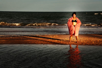 Woman wearing biking and fur coat while standing at beach during dusk