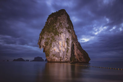 Rock formation in sea against sky at sunset