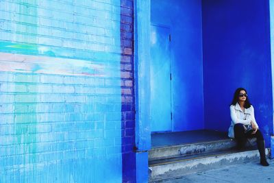 Young woman sitting against blue wall