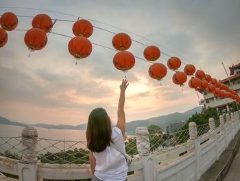 Rear view of woman with arm raised towards chinese lanterns against sky