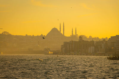 Silhouette buildings by sea against sky during sunset