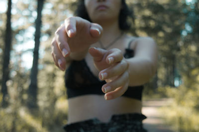 Midsection of young woman gesturing while standing in forest