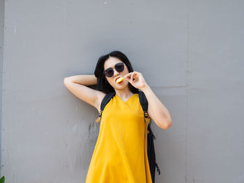 Portrait of young woman wearing sunglasses standing against wall