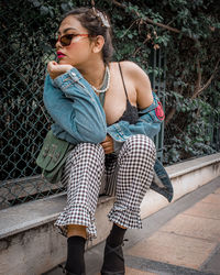 Full length of young woman wearing sunglasses sitting outdoors