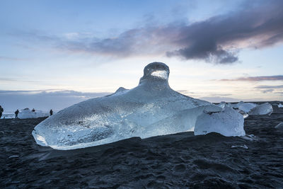 Iceberg on sand at beach against sky during sunset