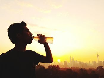 Young man drinking water from bottle against orange sky