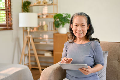 Portrait of young woman using mobile phone while sitting on sofa at home