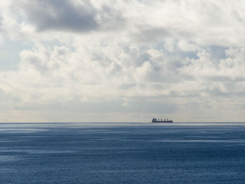 Scenic view of sea against sky with a cargo ship over the horizon