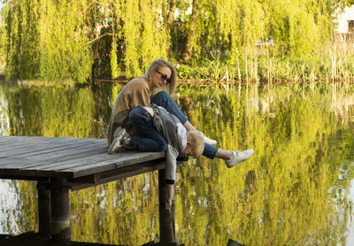 White mother and son sit on wooden dock enjoying lake view in summer time. child throws rocks into