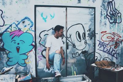 Side view of man standing against graffiti wall