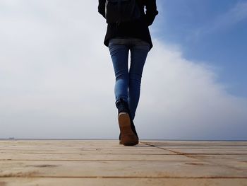 Low section of woman walking on pier against cloudy sky