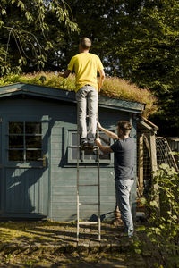 Father standing on ladder being supported by son in front of house