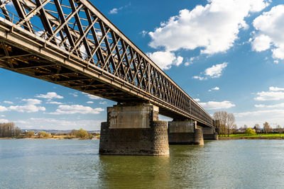 Steel, lattice structure of a railway bridge over a river with a background of blue sky with  clouds