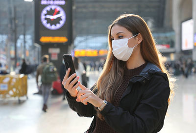 Young woman wearing mask using smart phone while standing on road