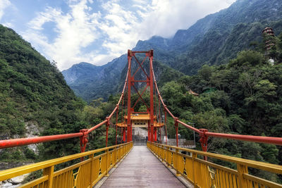 Footbridge leading towards mountains against sky