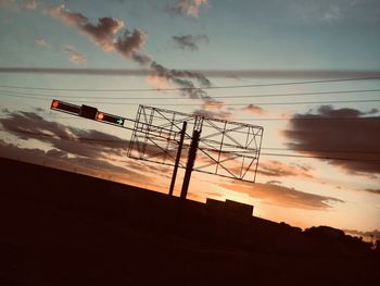 Low angle view of silhouette electricity pylon against sky during sunset