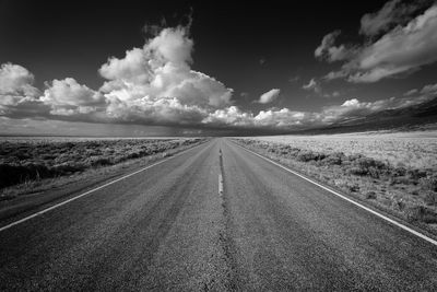 Empty road amidst field against sky