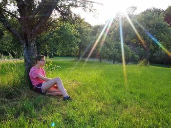 Side view of teenage girl sitting by tree on grassy field