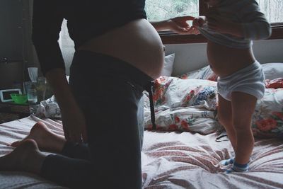 Low section of pregnant woman and baby boy on bed