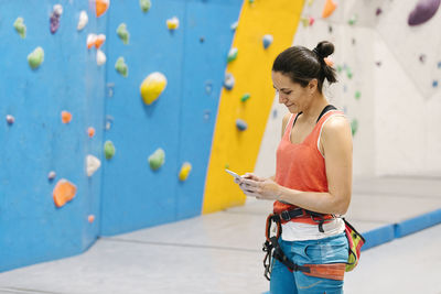 Woman using mobile phone against climbing wall