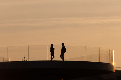 Silhouette people standing by railing against sky during sunset