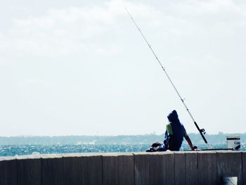 Man fishing in sea against sky