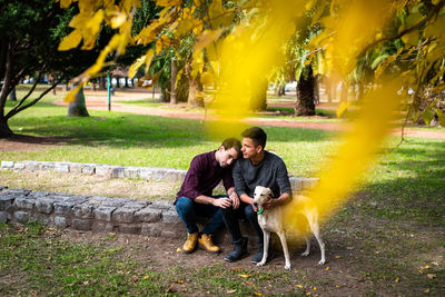 Full length of gay couple with dog sitting at park