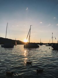 Sailboats moored on sea against sky during sunset